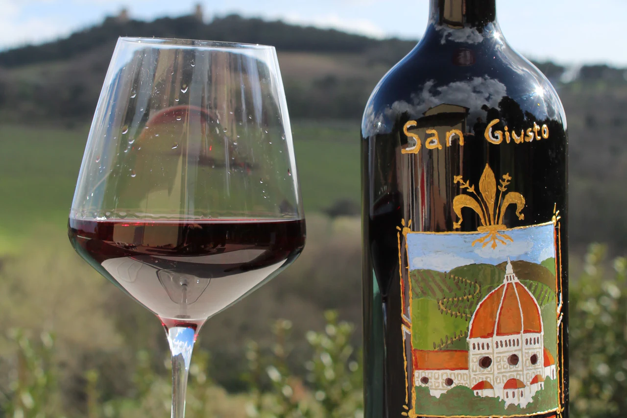 Un calice di rosso e una bottiglia San Giusto con le colline sullo sfondo
